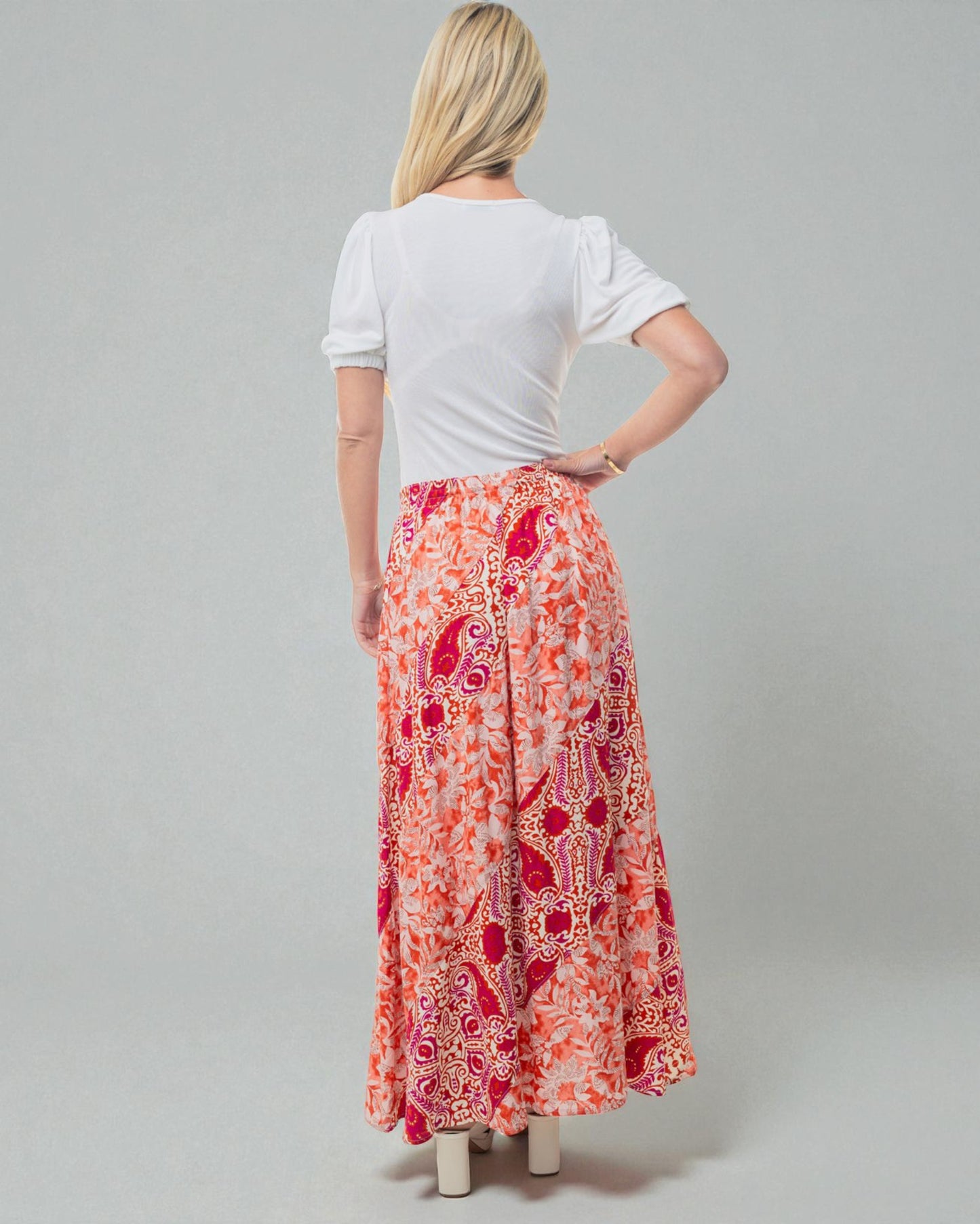 Woman wearing a white top and a long, patterned orange and red skirt on a gray background