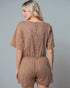 Woman wearing a brown tie-dye romper against a gray background