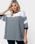 A woman modeling a loose, oversized short-sleeve top with a color-blocked design featuring vertical black and white stripes on the lower half, solid white on the upper chest and shoulders, and solid black trim at the neckline and sleeve cuffs.