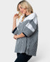 A woman modeling a color-blocked top with vertical black and white stripes on the body and sleeves, solid white shoulder panels, and black trim, against a light gray studio background.