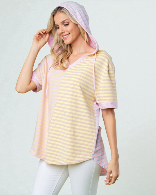 Woman wearing a yellow and pink striped shirt with a matching hood on a light gray background