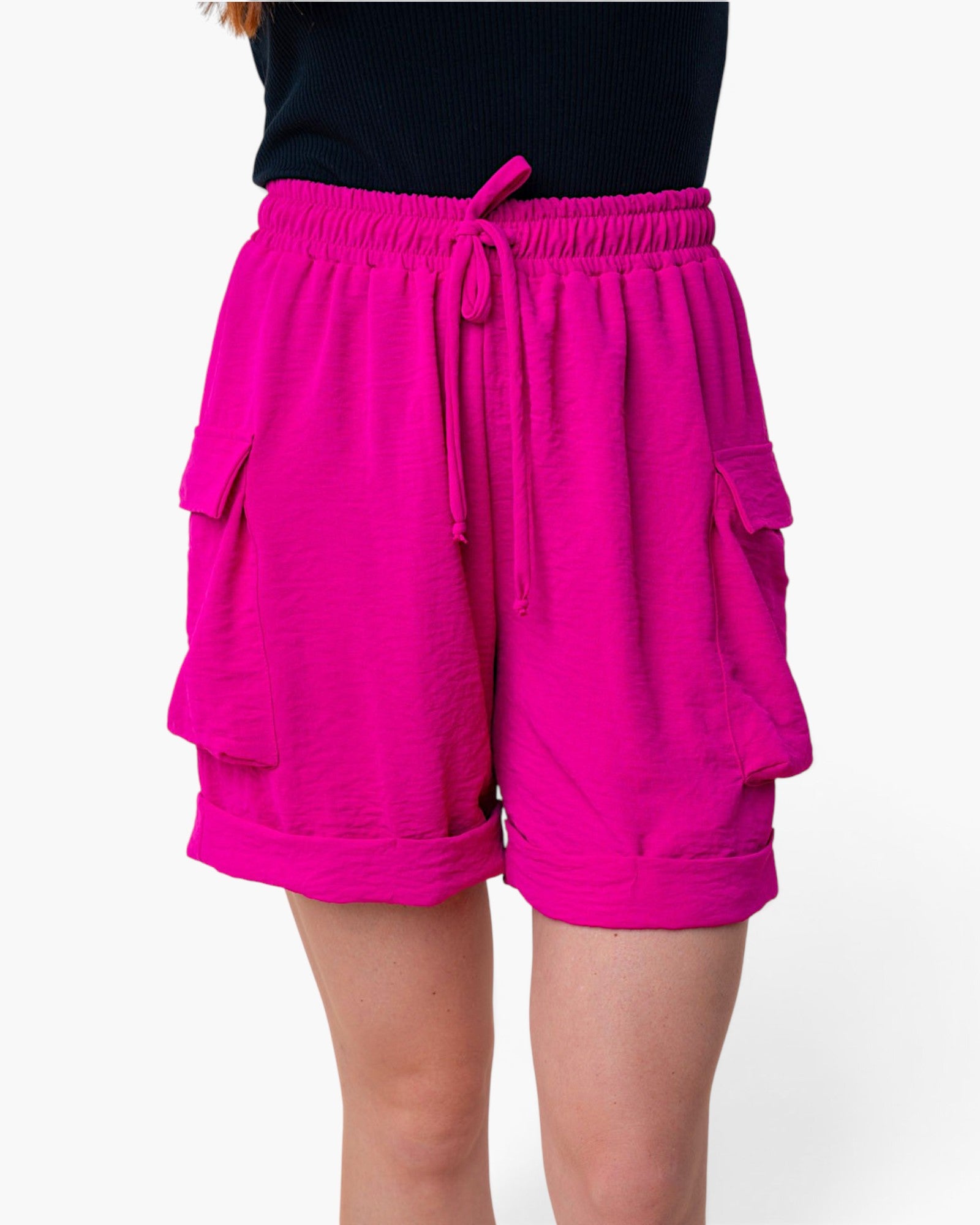 Bright pink cargo shorts with a drawstring waist and side pockets, shown on a model from the waist down against a plain white background.