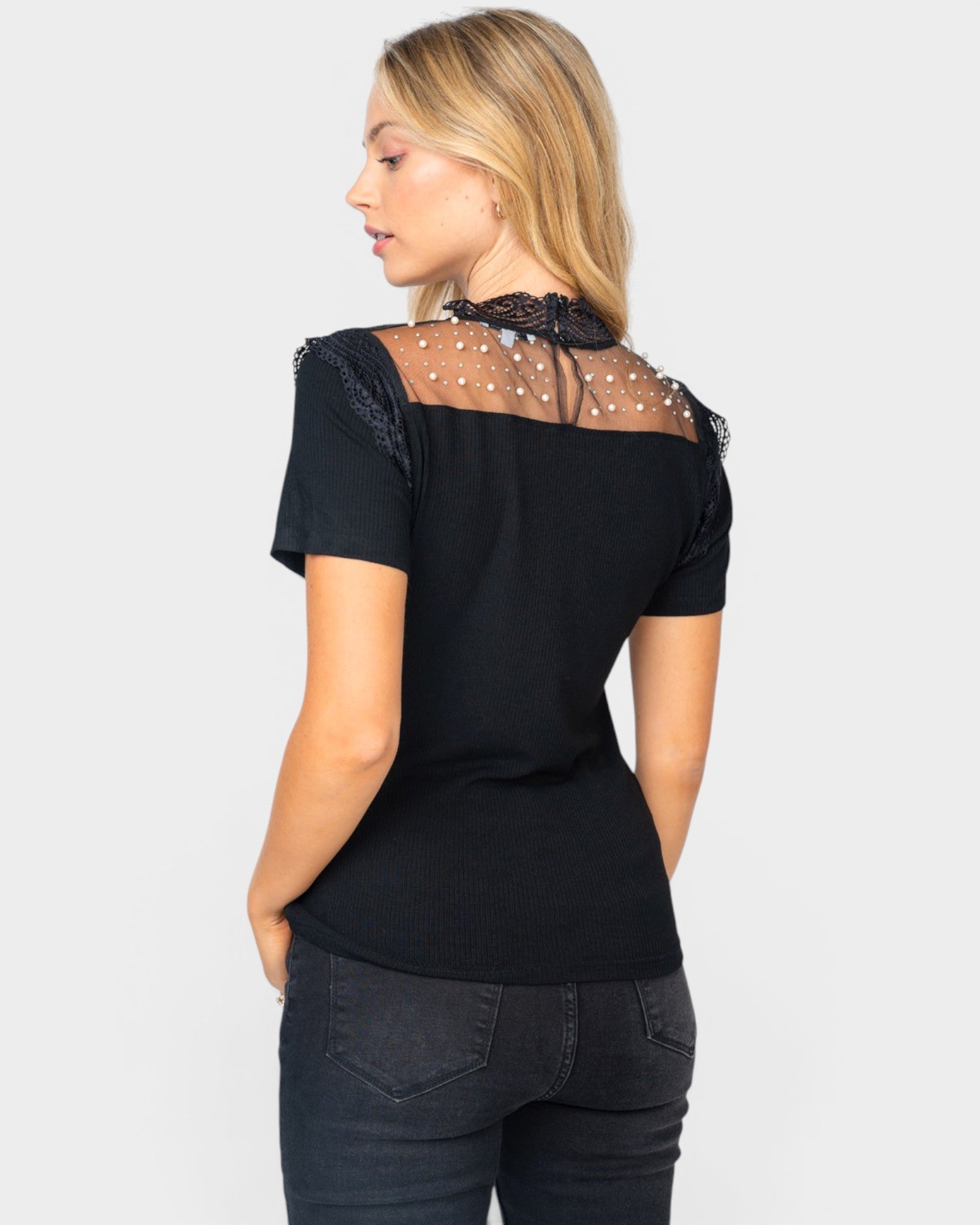 Woman wearing a black top with sheer sleeves and mesh back on a white background