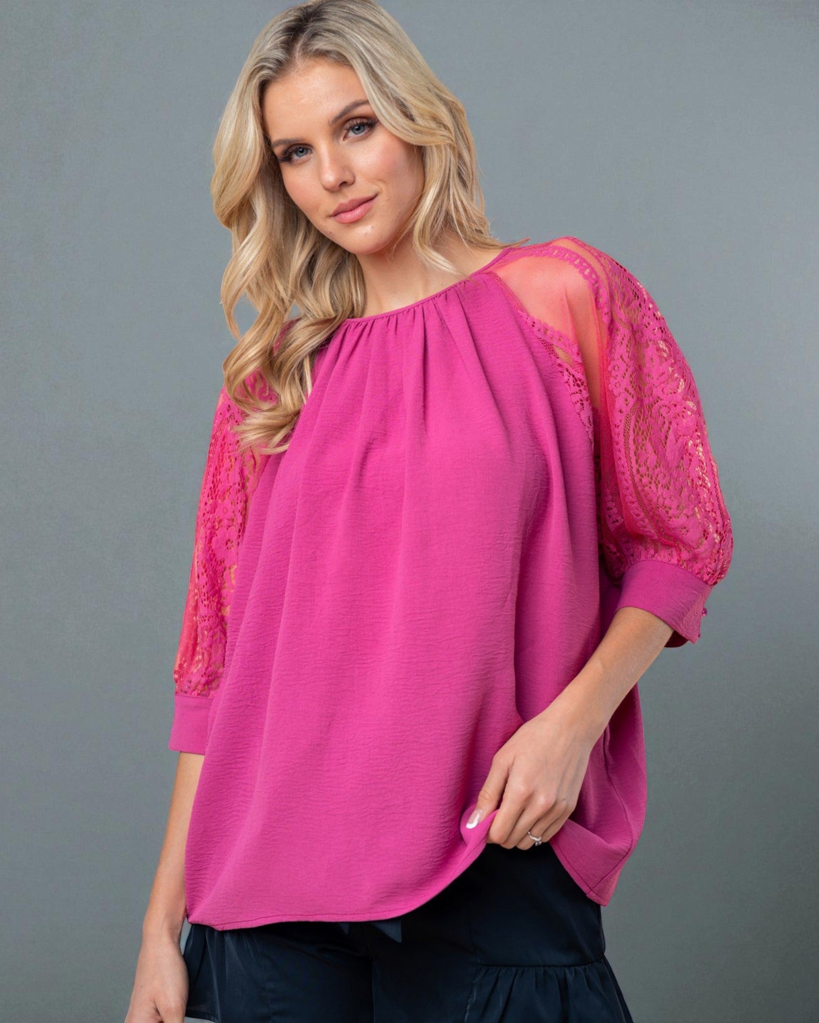 Woman wearing a pink blouse with lace sleeves against a gray background