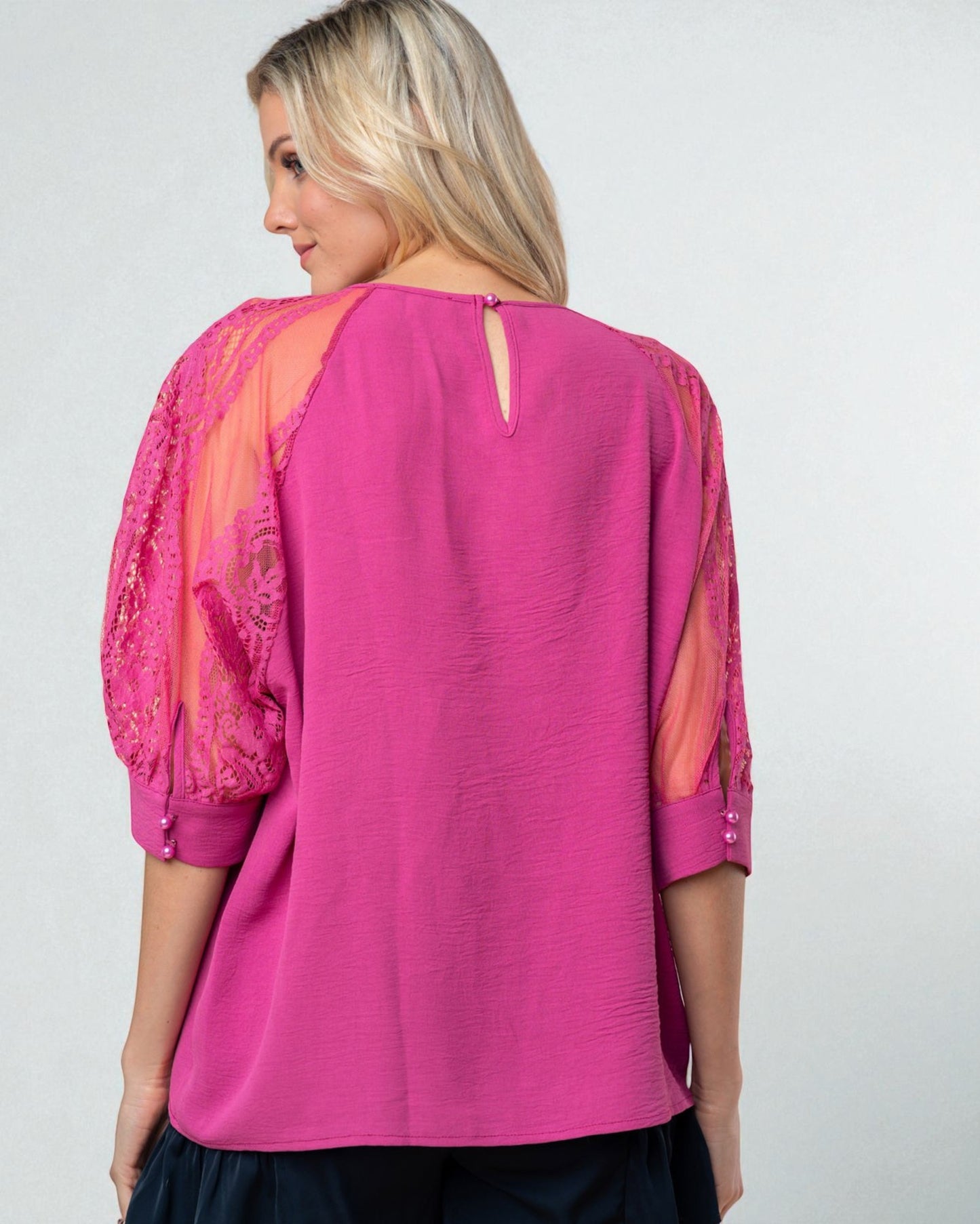 Woman wearing a pink blouse with sheer sleeves on a white background