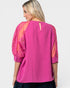 Woman wearing a pink blouse with sheer sleeves on a white background