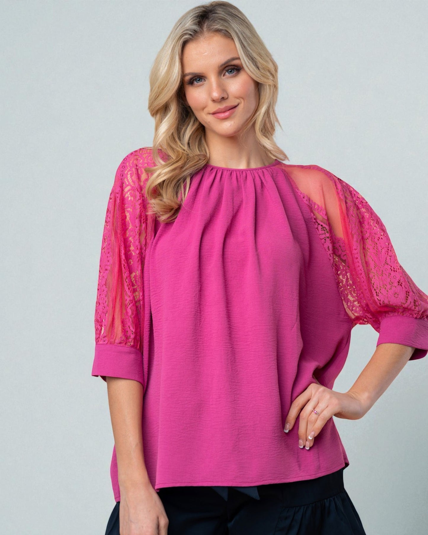 Woman wearing a pink blouse with lace sleeves on a gray background