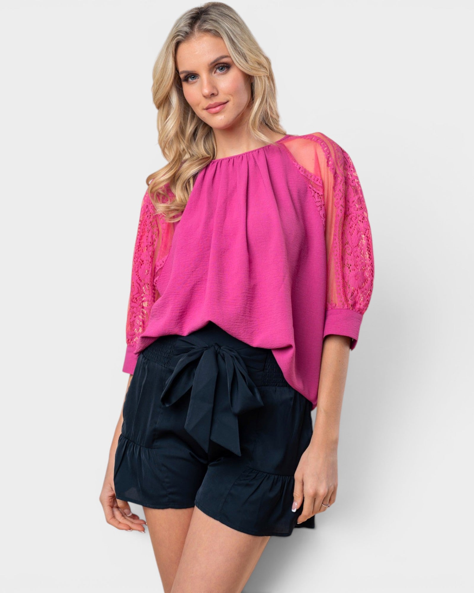 Woman wearing a pink blouse with lace sleeves and black shorts on a white background