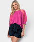 Woman wearing a pink blouse with lace sleeves and black shorts on a white background