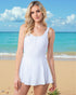 Woman in a white dress standing on a beach with blue ocean and sky.