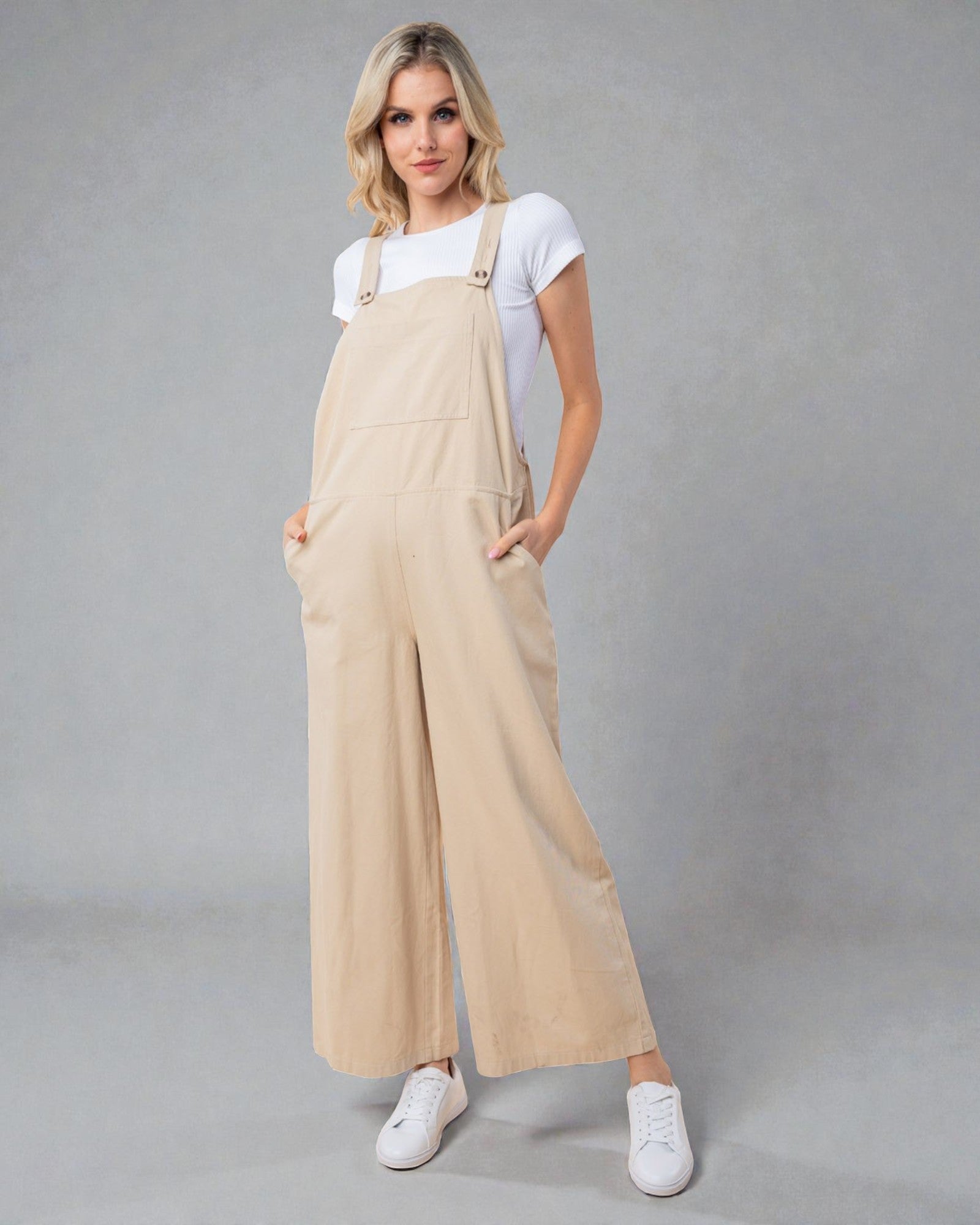 Woman wearing beige overalls and white sneakers on a gray background