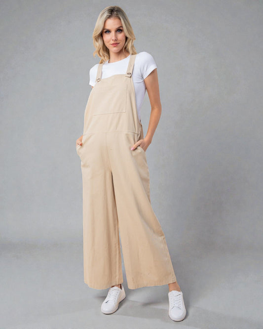 Woman wearing beige overalls and white sneakers on a gray background