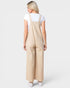 A woman shown from the back wearing beige wide-leg overall jumpsuit over a white t-shirt, on a light gray studio background.