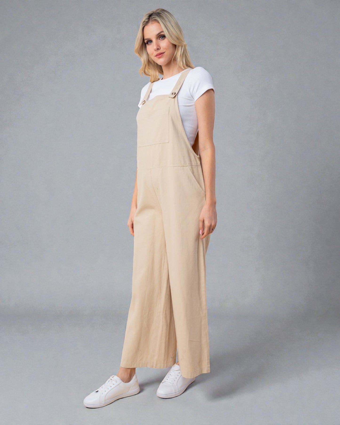 Woman wearing beige overalls and white sneakers on a gray background