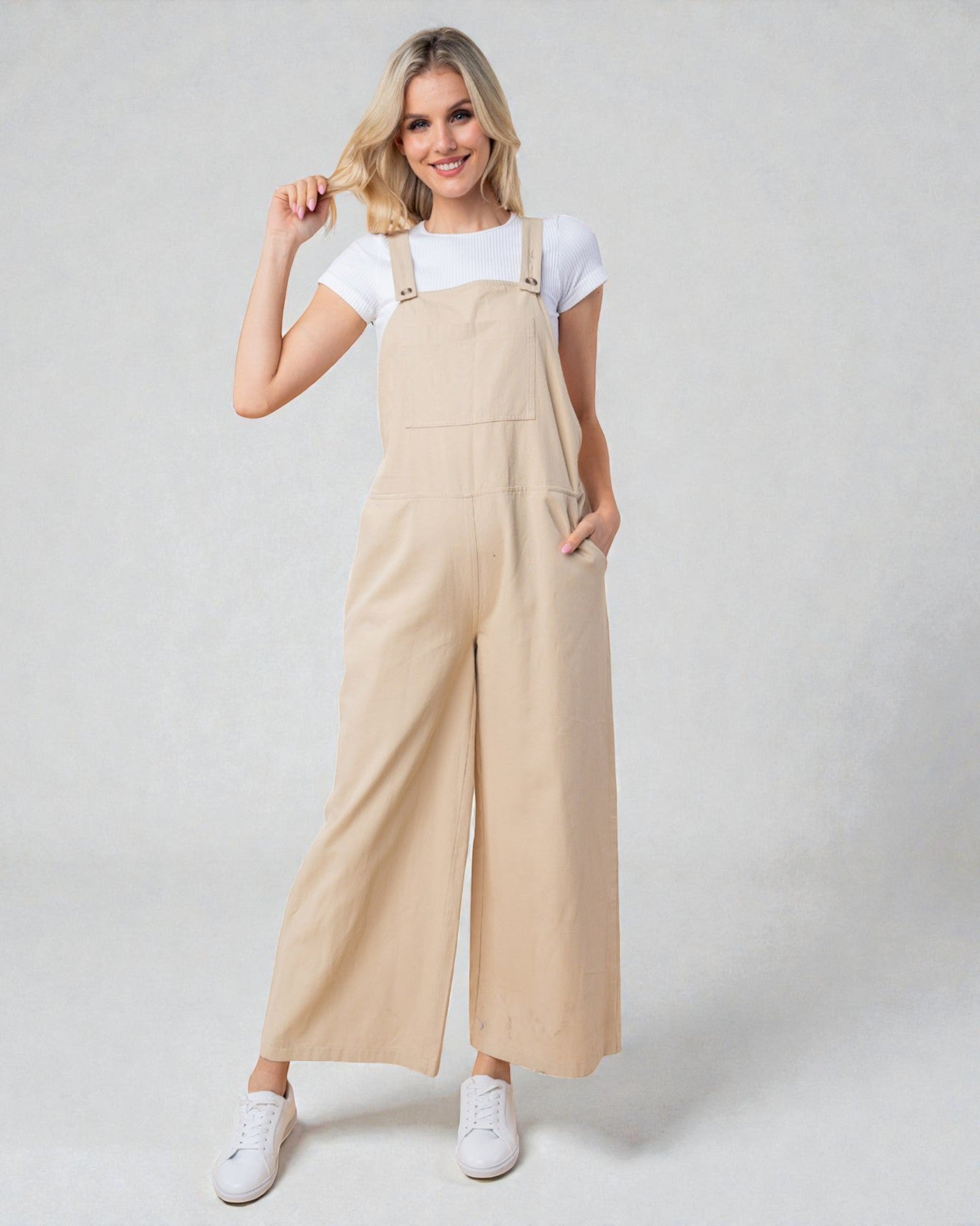 Woman wearing beige overalls and white sneakers on a plain background