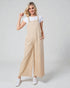 Woman wearing beige overalls and white sneakers on a plain background