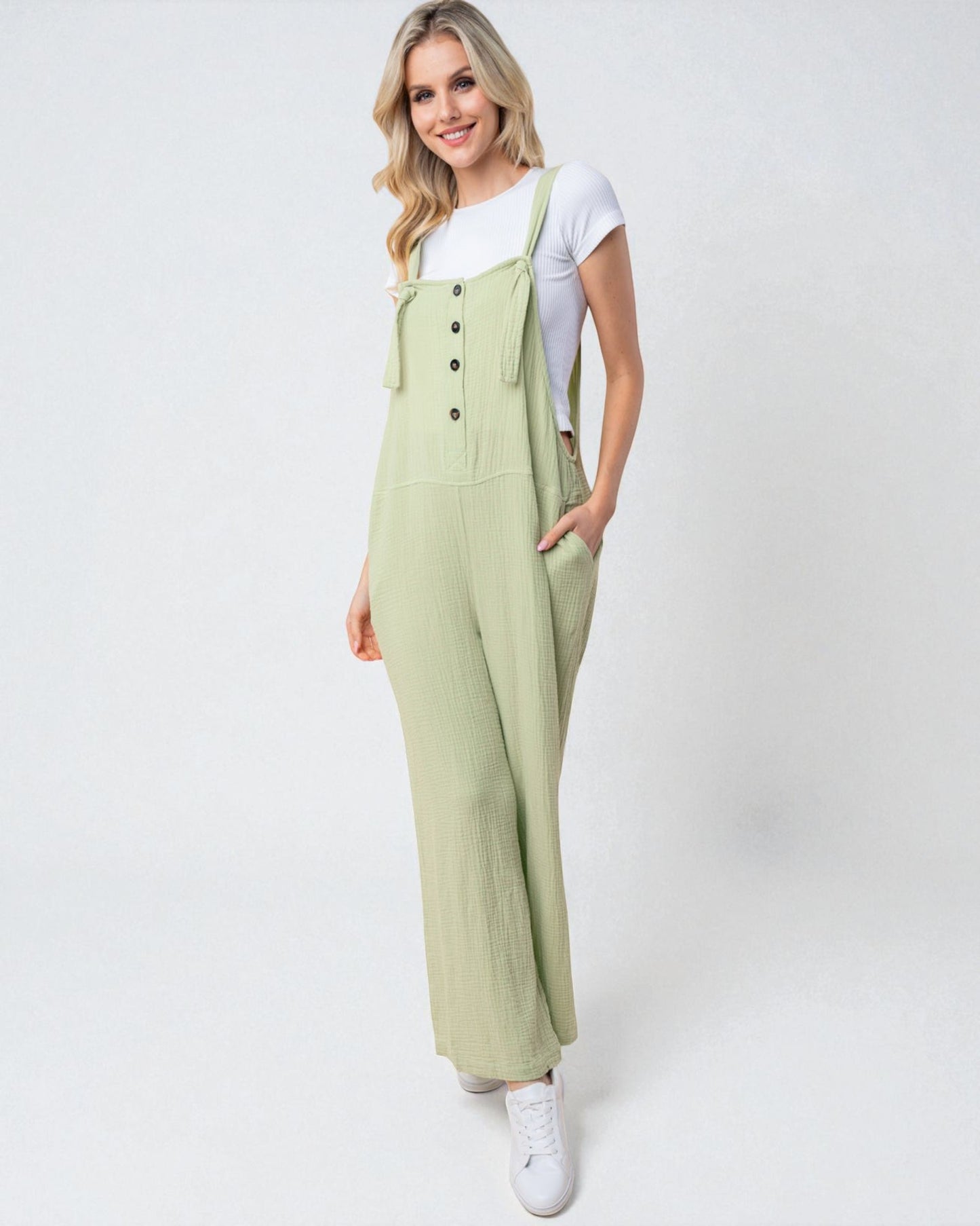 Woman wearing a light green jumpsuit with white sneakers on a white background