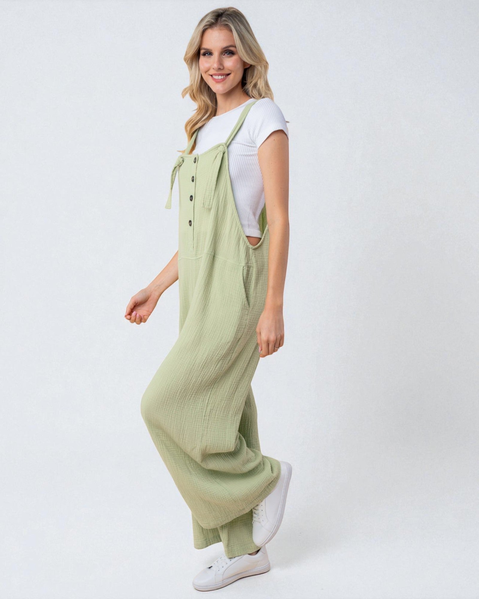 Woman wearing a green jumpsuit and white sneakers on a white background