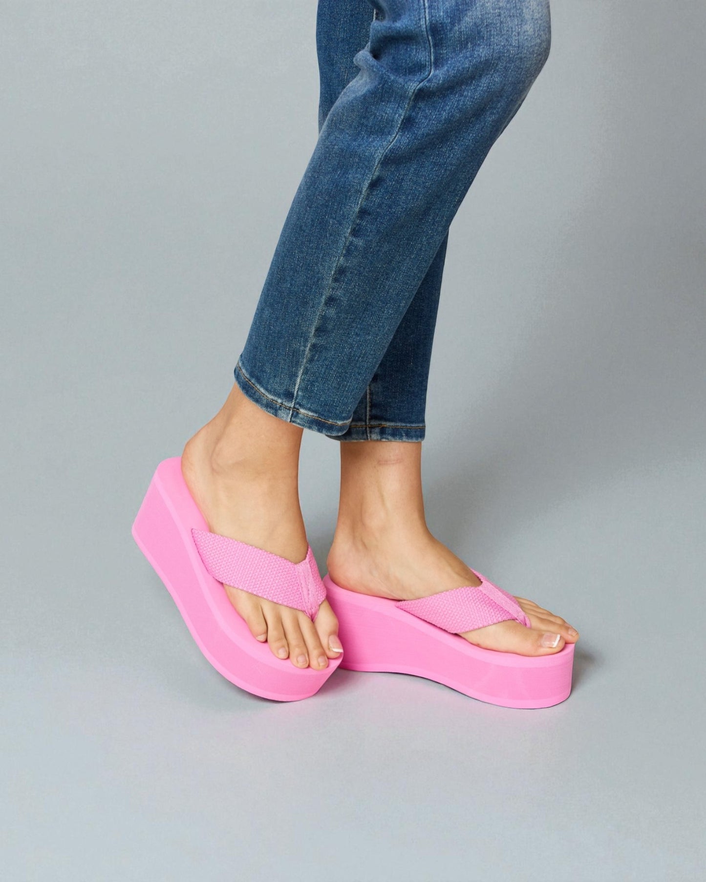 Person wearing bright pink platform sandals with blue jeans on a gray background