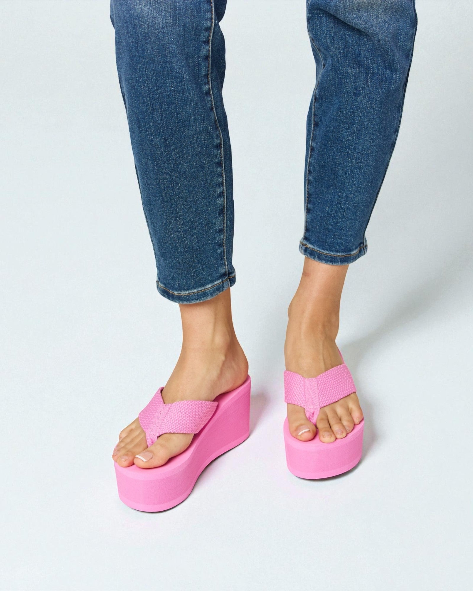 Person wearing bright pink platform sandals with blue jeans on a white background