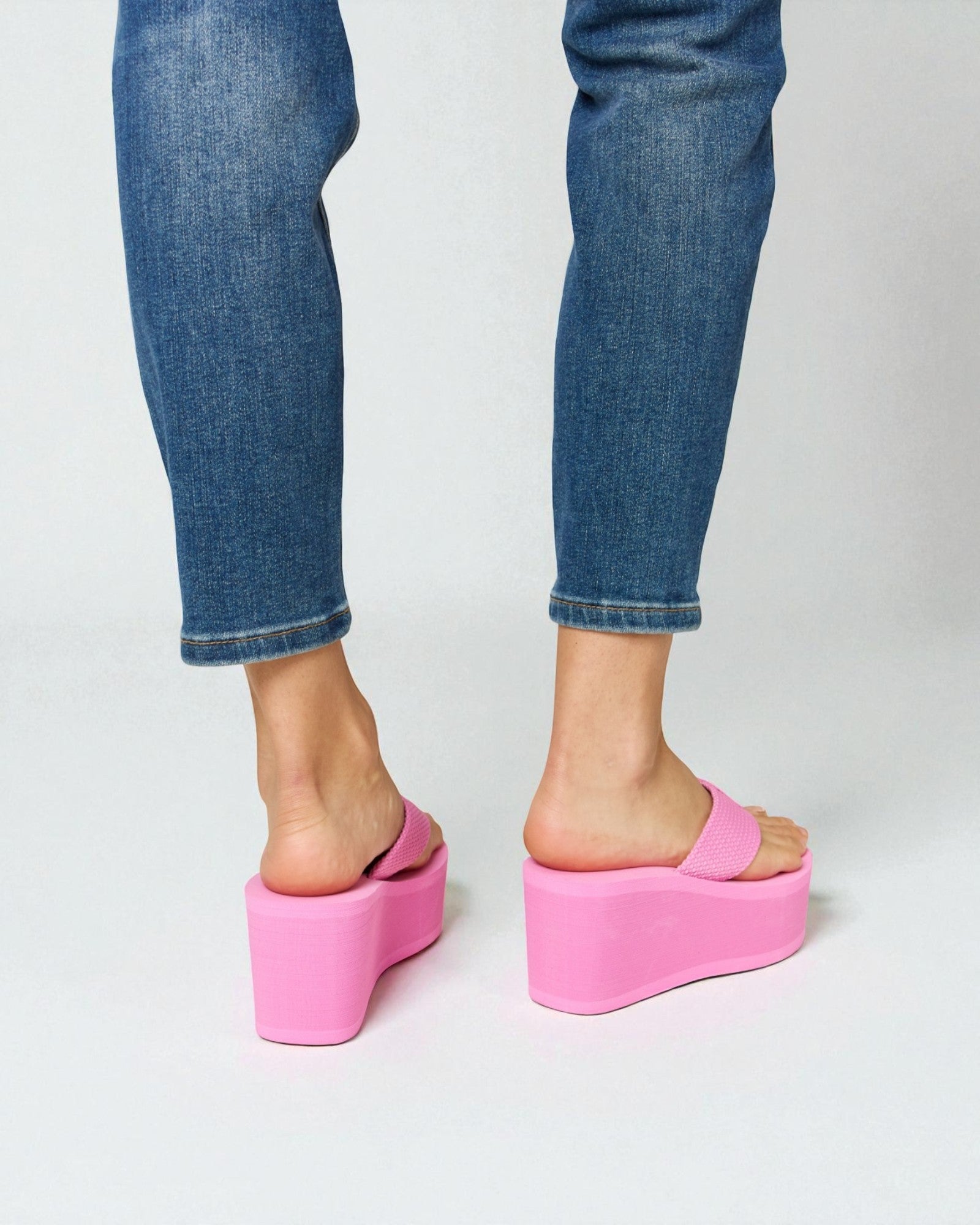 Person wearing blue jeans and pink platform sandals on a white background