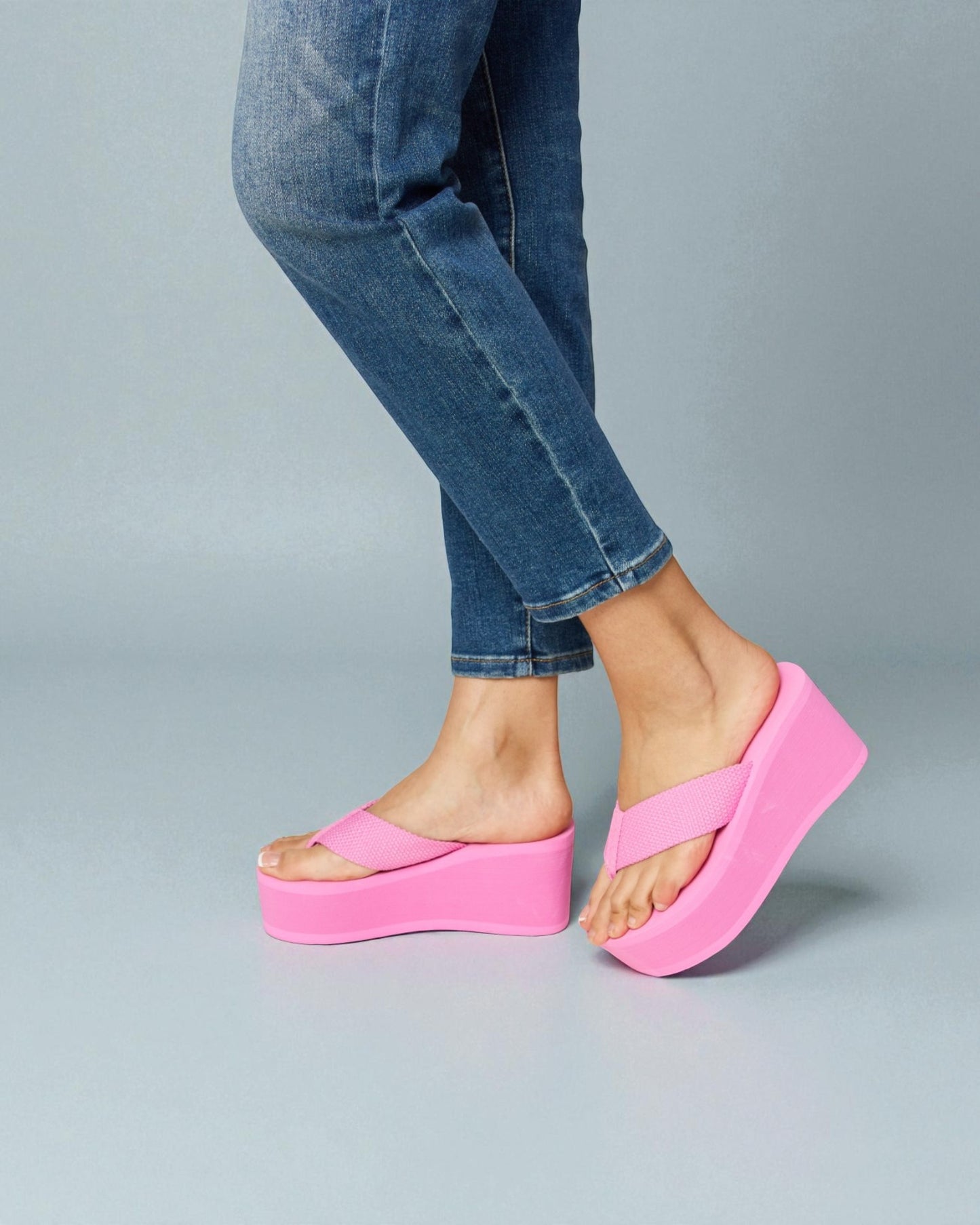 Person wearing bright pink platform sandals with blue jeans on a gray background