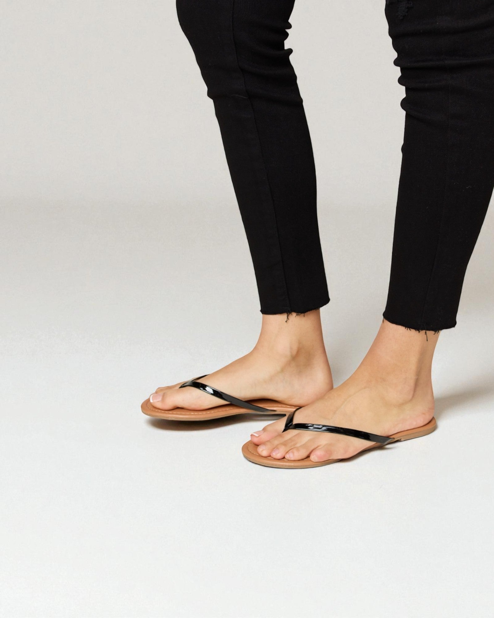 Person wearing black sandals and black pants on a white background