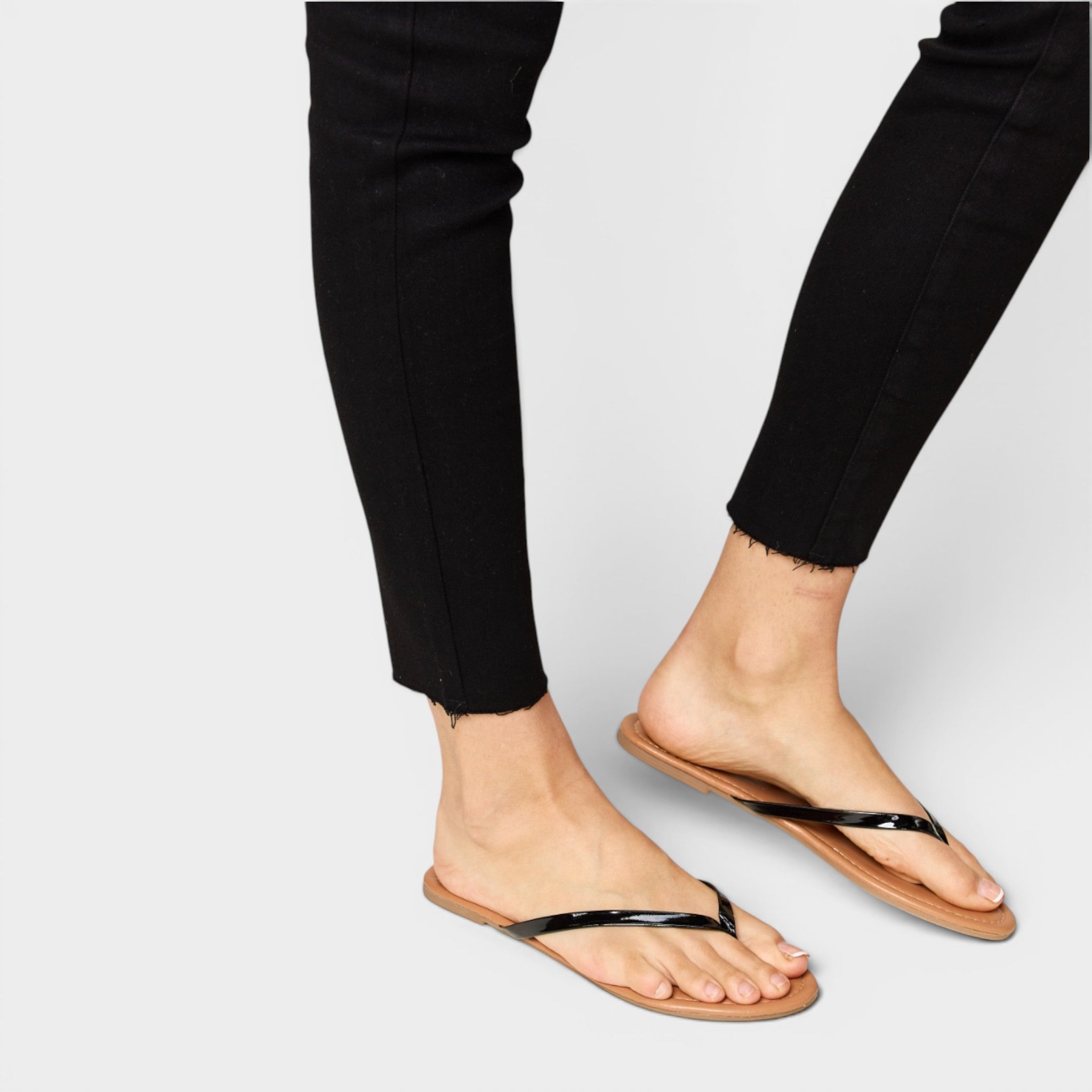 Person wearing black pants and tan sandals with black straps on a light gray background
