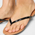 Close-up of a foot wearing a tan sandal with a black strap on a light gray background