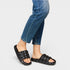 Person wearing black quilted sandals with blue jeans on a light gray background