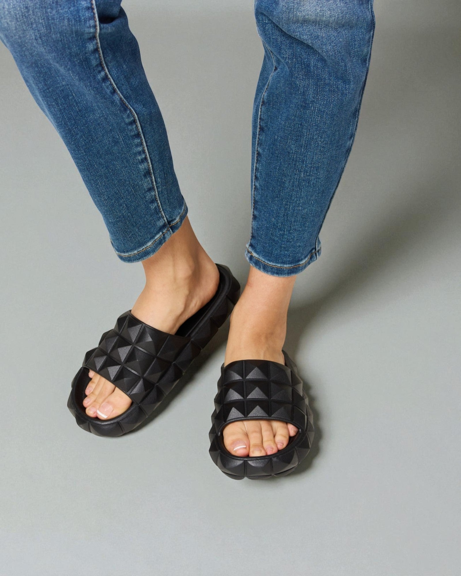 Black quilted sandals worn with blue jeans on a gray background