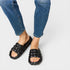 Black quilted sandals worn with blue jeans on a light gray background