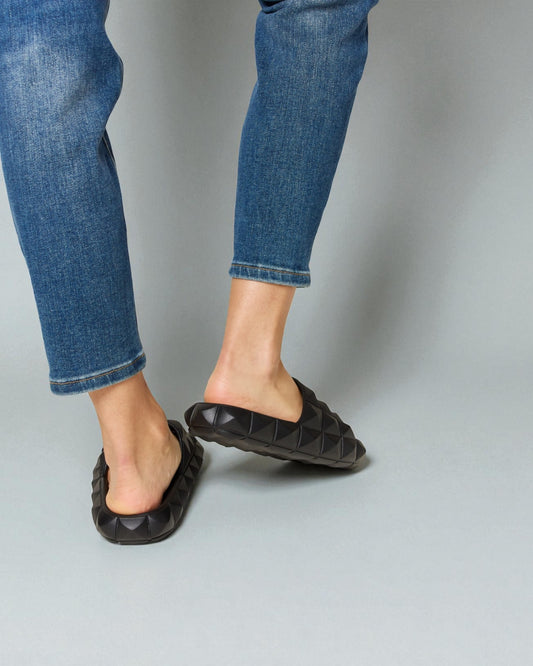 Person wearing blue jeans and black flat shoes on a gray background