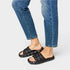 Black quilted sandals worn with blue jeans on a light gray background