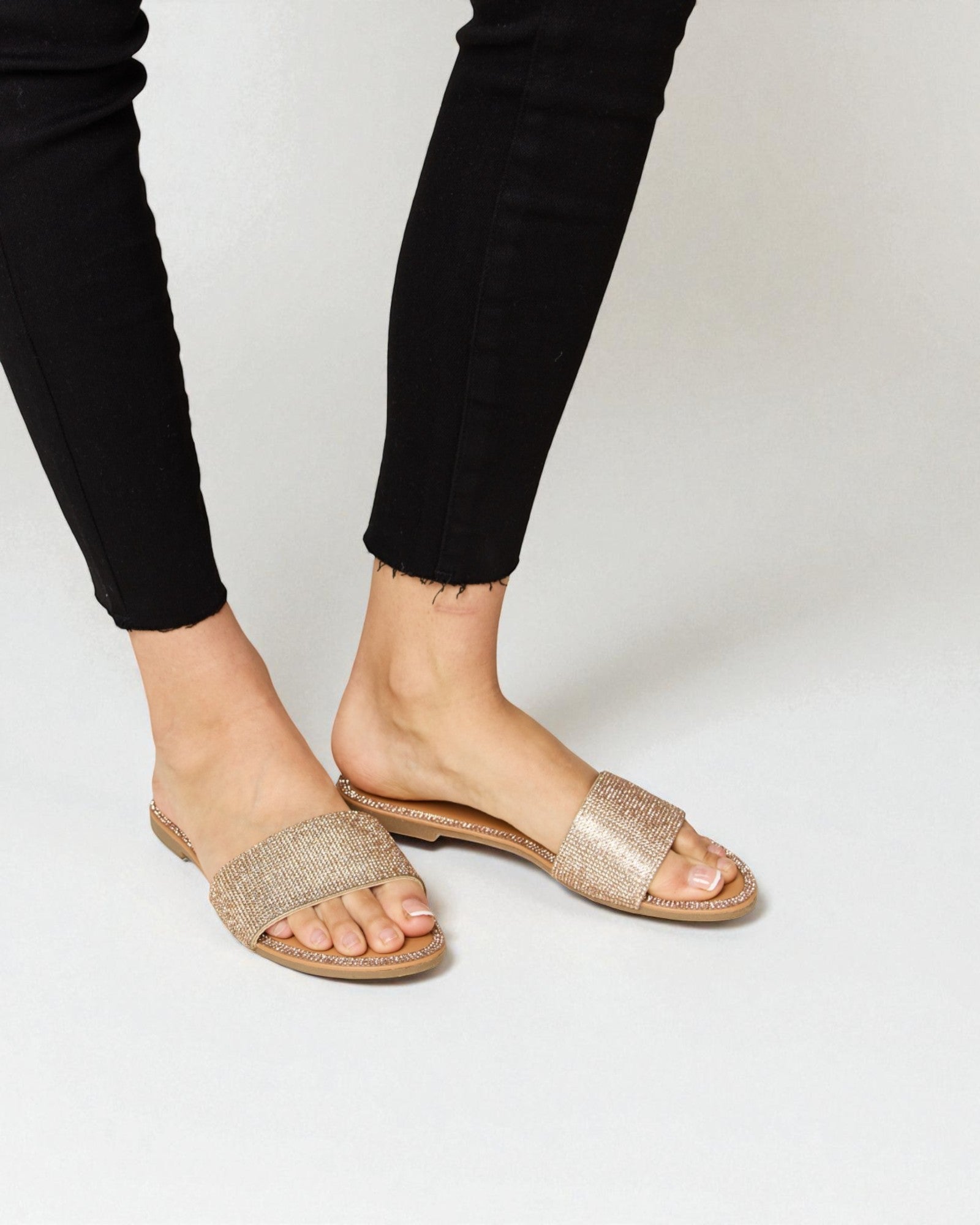 Gold glitter sandals worn with black pants on a plain background