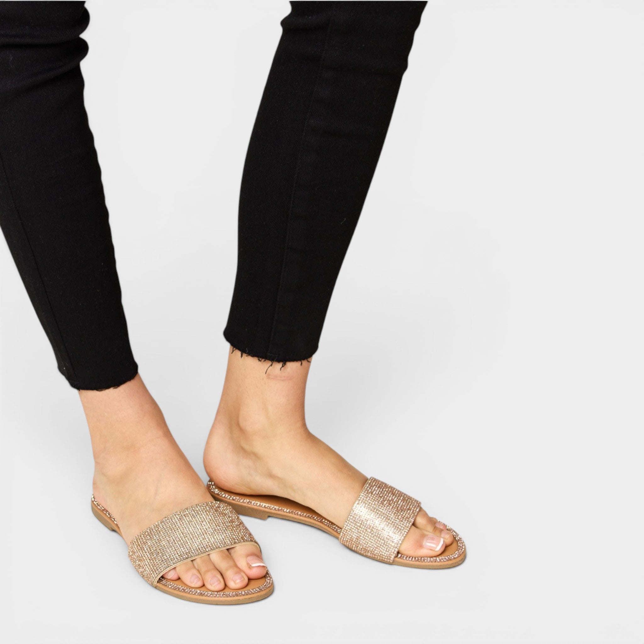 Gold glitter sandals worn with black pants on a plain background