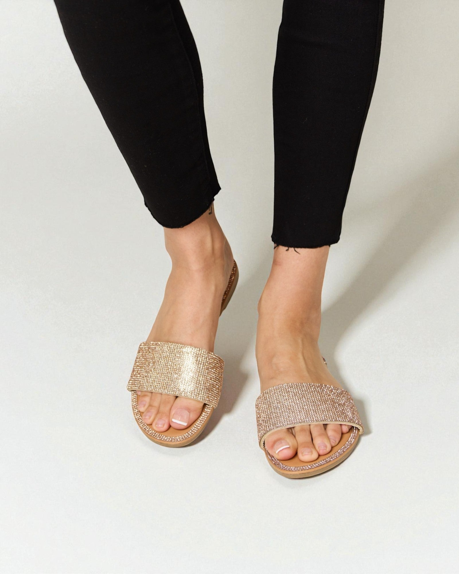 Gold sandals worn with black pants on a white background