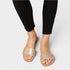 Gold sandals worn with black pants on a light gray background