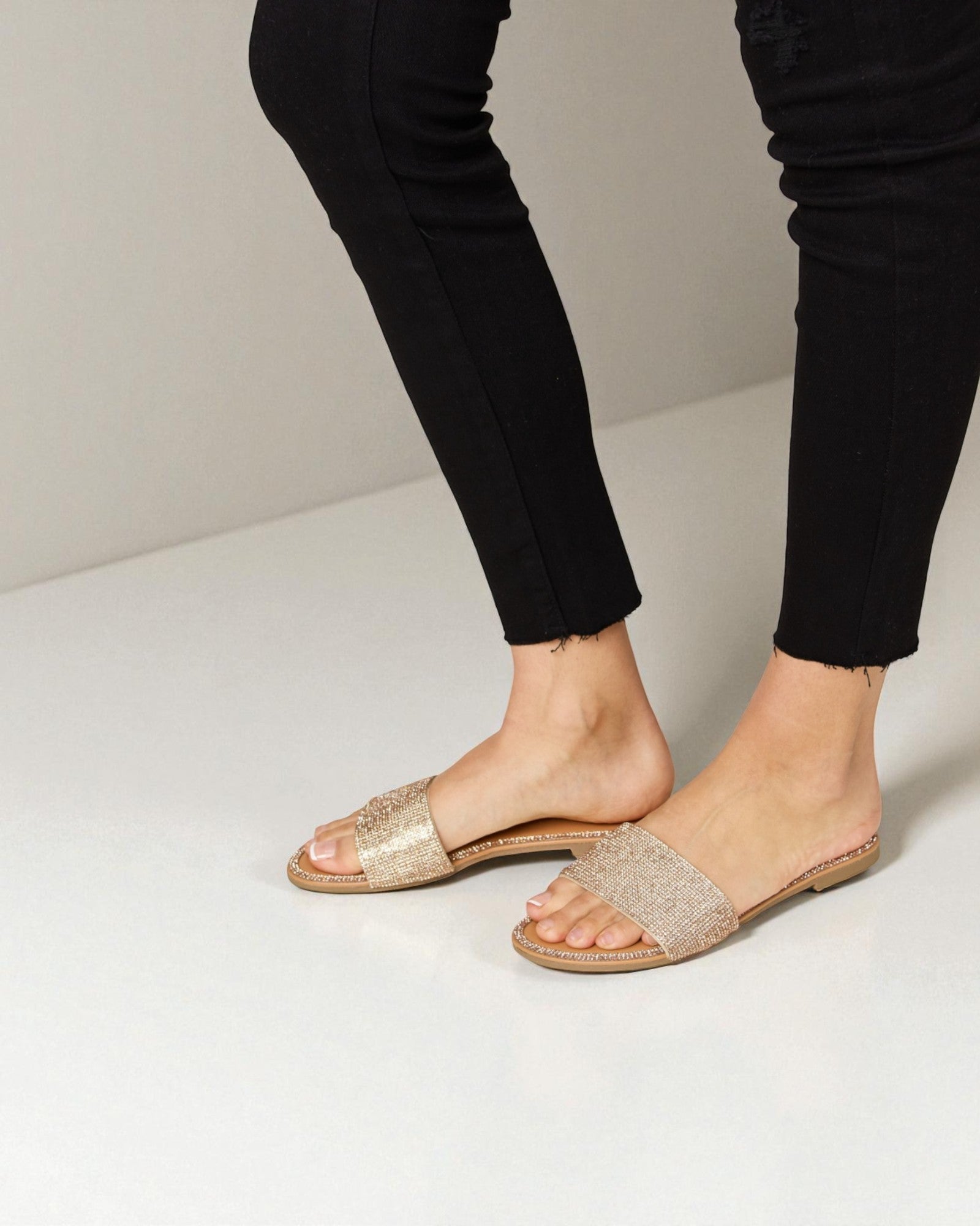 Gold sandals worn with black pants on a light background