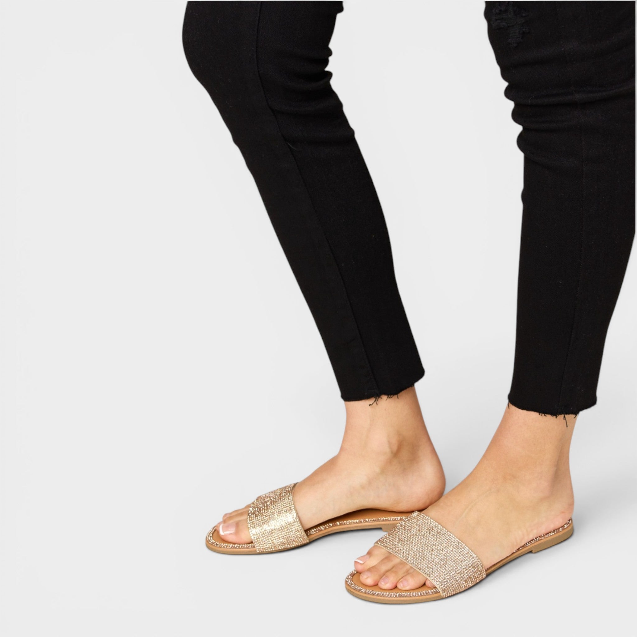 Gold sandals worn with black pants on a light gray background