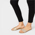 Gold sandals worn with black pants on a light gray background