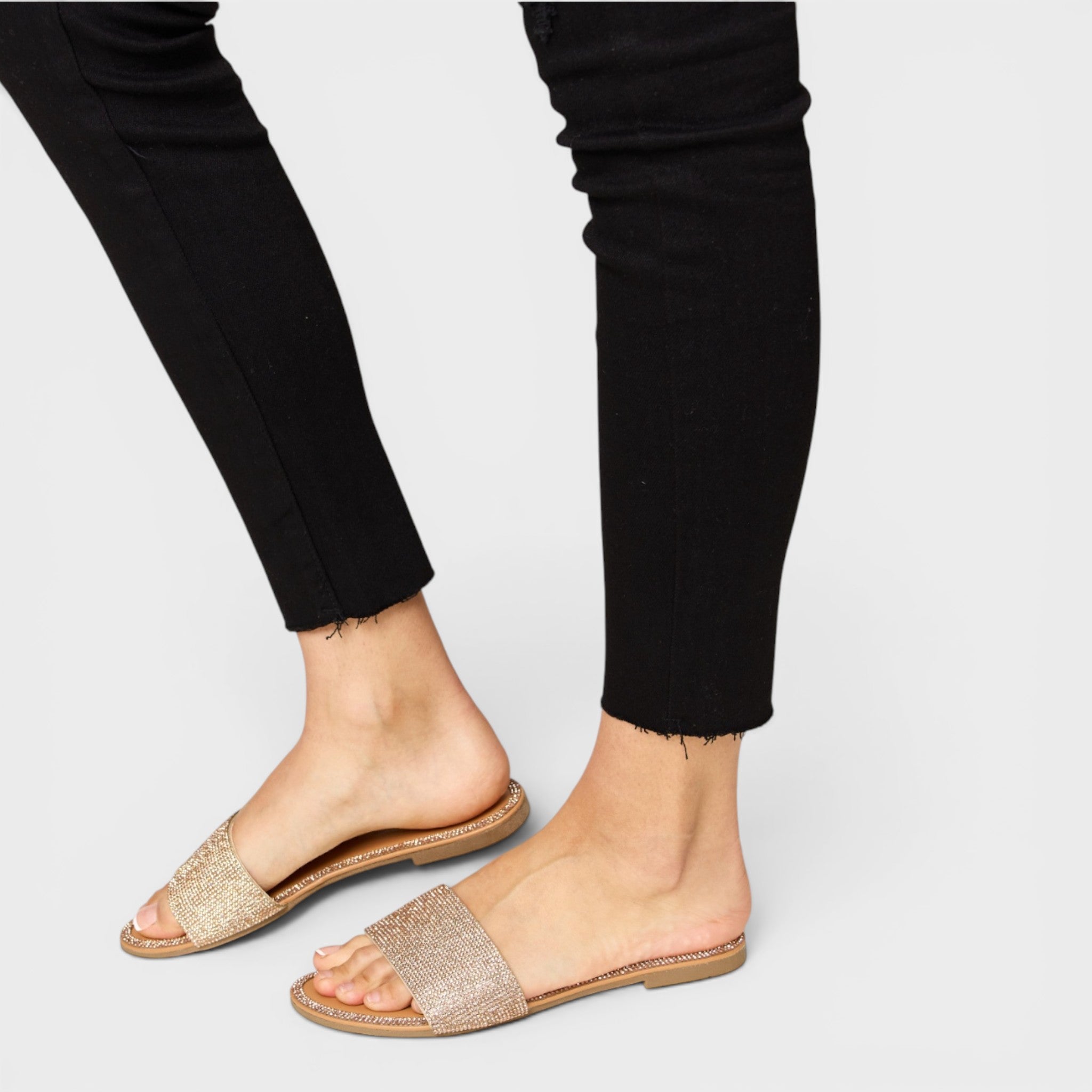 Gold open-toe sandals worn with black pants on a light gray background