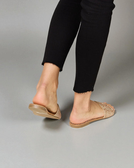 Person wearing gold glittery sandals on a gray background