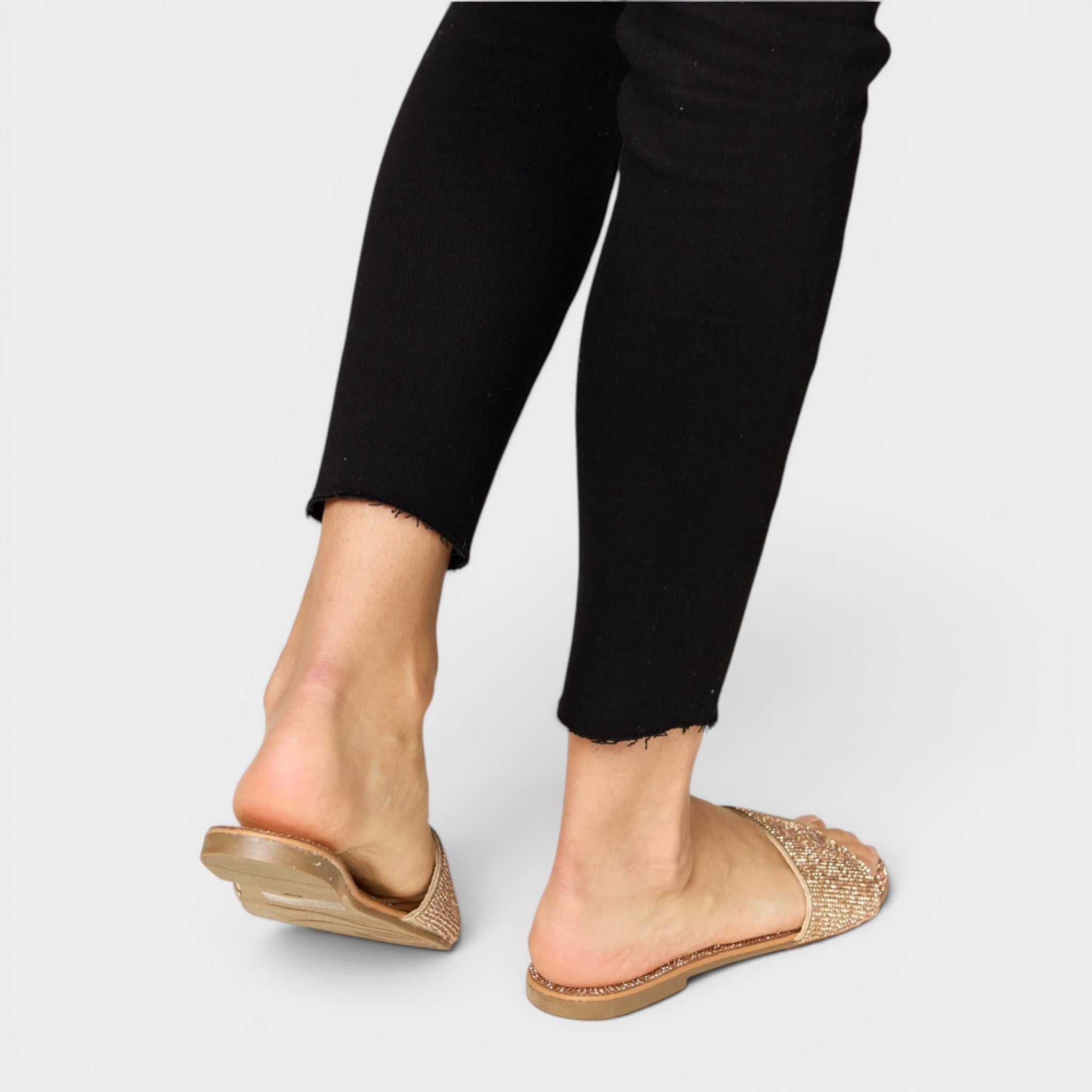 Gold open-toe shoes worn with black pants on a light gray background