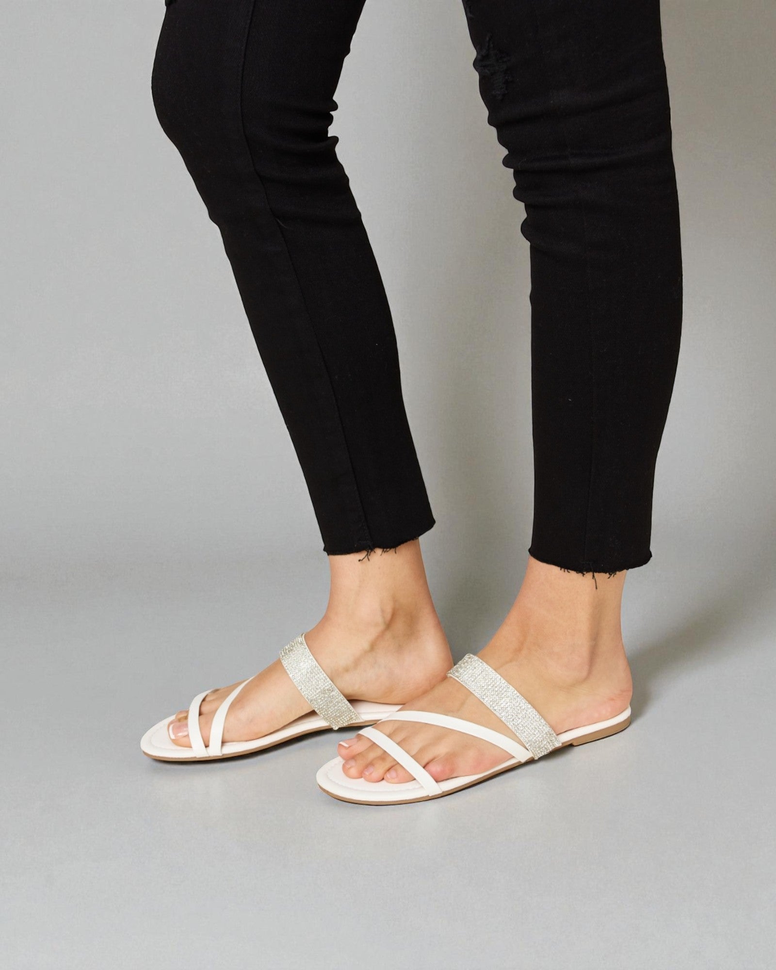 White sandals worn with black pants on a gray background