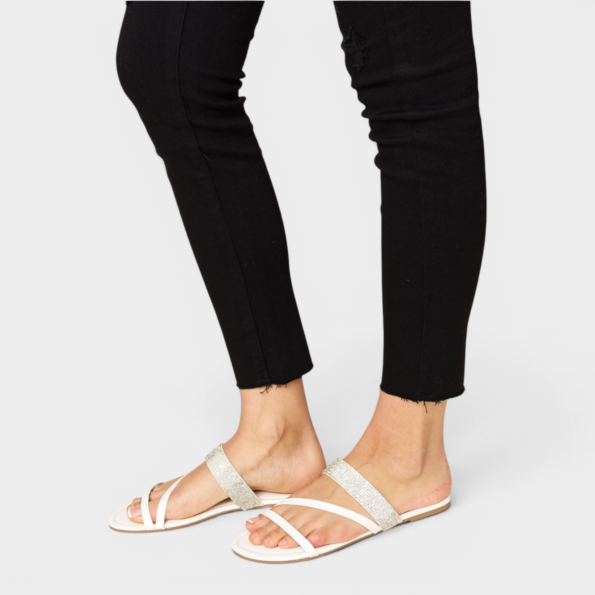White sandals worn with black pants on a plain background