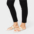 White sandals worn with black pants on a plain background