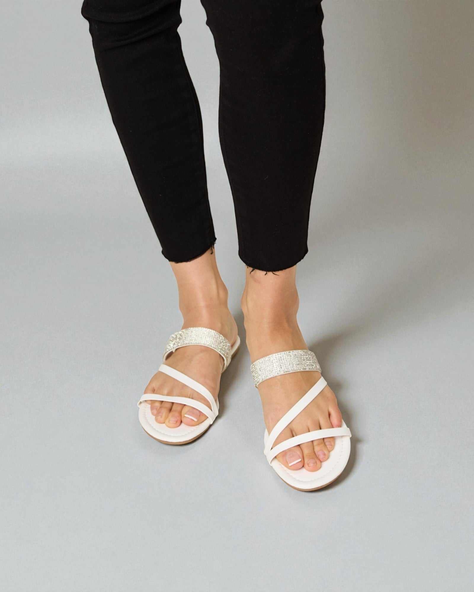 White sandals worn with black pants on a gray background