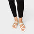 White sandals with glittery straps worn with black pants on a light gray background