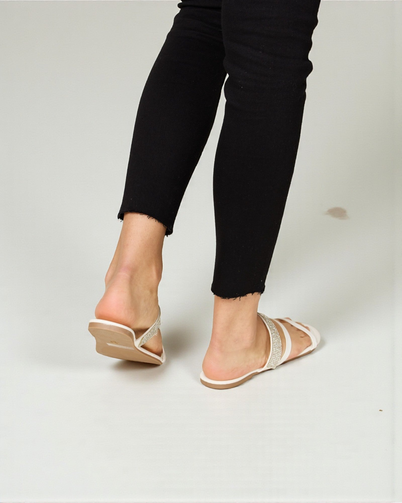 Person wearing black pants and gold sandals on a white background